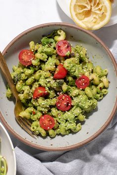 a bowl filled with guacamole and tomatoes next to a plate of lemon wedges