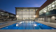 an empty swimming pool in front of a large building with glass walls and stairs leading up to it