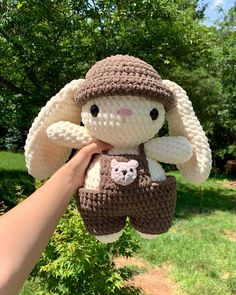 a hand holding a small stuffed animal in the shape of a bunny wearing a hat