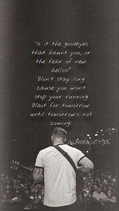 a man standing in front of a crowd with a guitar and poem written on it