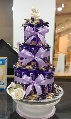 a tiered cake made out of chocolates and wrapped in purple ribbon with flowers on top