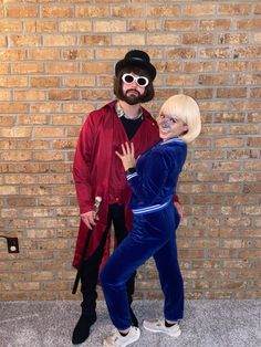 a man and woman dressed in costumes standing next to a brick wall with their arms around each other