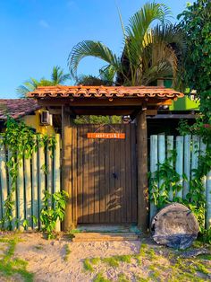 a wooden gate in front of a fence with plants growing on it and a rock