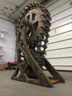 an old metal gear wheel sitting on top of a cement floor next to a garage door