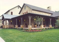 a large house with an attached porch and stone pillars on the front lawn, surrounded by lush green grass