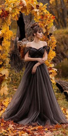 a woman in a black dress standing under an archway with leaves on the ground around her