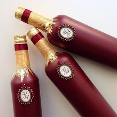 three red bottles with gold trim and monogrammed labels on them are sitting next to each other