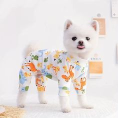 a small white dog standing on top of a bed wearing pajamas and looking at the camera