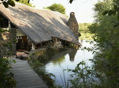 a house with a thatched roof next to a body of water in the woods