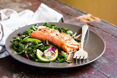 a plate with salmon, greens and lemon wedges on it next to a fork