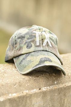 a camo hat with the letters tx on it sitting on top of a stone wall