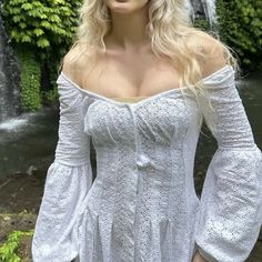 a woman with blonde hair wearing a white dress in front of a waterfall and trees