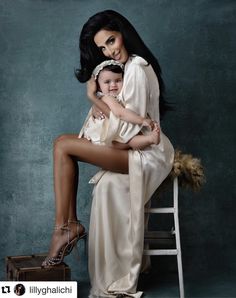 a woman holding a baby sitting on top of a wooden chair next to a suitcase