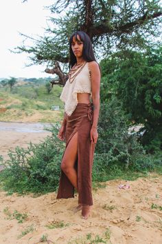 a woman standing on top of a sandy beach next to a green tree and bushes