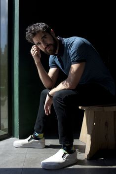 a man sitting on top of a wooden bench next to a window with his hand under his chin