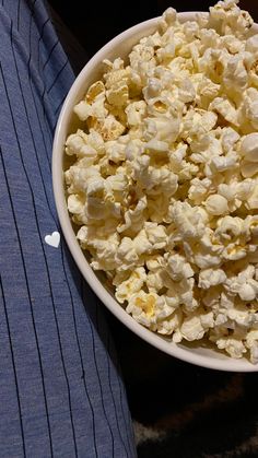 a white bowl filled with popcorn sitting on top of a table next to a blue shirt