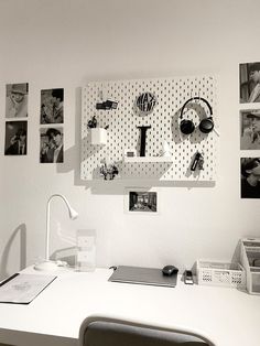 a white desk topped with a computer monitor next to a wall covered in pictures and headphones