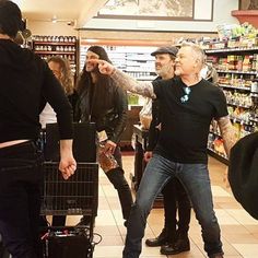 a group of people in a store with one man pointing at the camera and another person holding a shopping cart