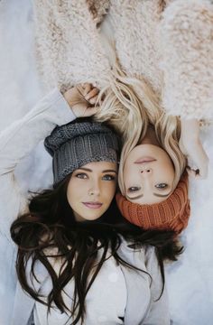 two women laying on top of each other wearing knitted hats and scarves with faces painted on them