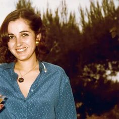 a woman is smiling and holding a drink in her hand while wearing a blue shirt