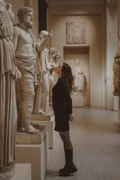 a woman standing in front of statues looking at something on the wall above her head