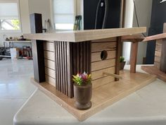 a wooden birdhouse with flowers in the center on a white countertop next to a window