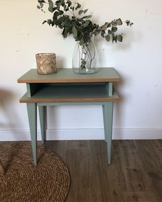 a small table with a vase on it next to a rug and a plant in a glass jar