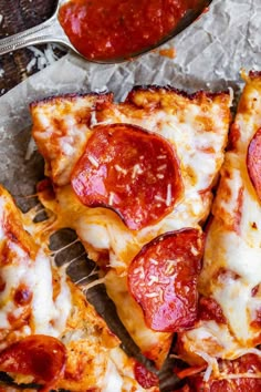 several slices of pepperoni pizza sitting on top of a piece of wax paper next to a spoon