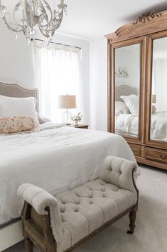 a bedroom with a white bed and chandelier in front of a large mirror