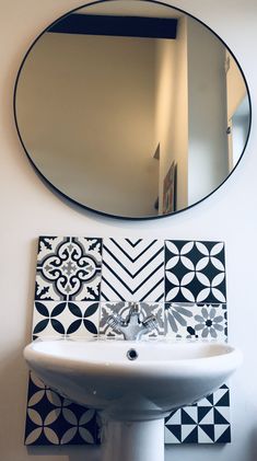 a white sink sitting under a round mirror next to a wall mounted faucet