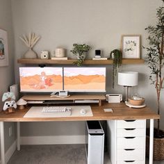 a computer desk with two monitors and a keyboard on top of it in front of a potted plant