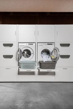 two washers and a dryer in a room with white cabinets on the wall