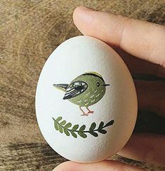 a hand holding an egg with a bird painted on it