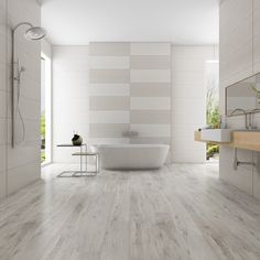 a bathroom with white walls and wood flooring, a tub in the middle is next to a sink