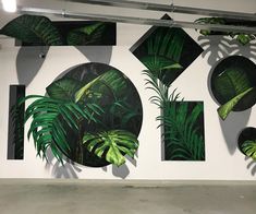 a white wall with some green plants and black circles on the wall above it is a painting of palm leaves