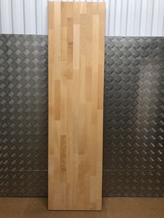 a large wooden cutting board sitting on top of a metal floor next to a wall