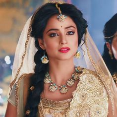 a woman in a bridal gown and jewelry looks at the camera with two other women behind her