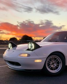 a white sports car parked in a parking lot with the sun going down behind it