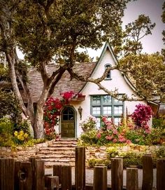 a white house with flowers around it and a wooden fence in the front yard area