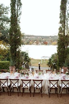 an outdoor dining table set up with white linens and pink centerpieces, surrounded by greenery