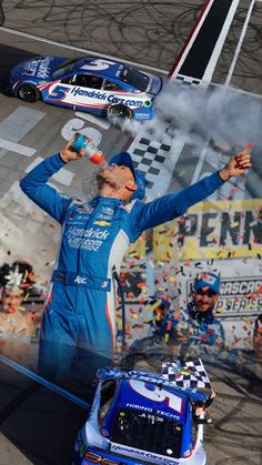 a man in blue racing suit standing on top of a race track next to a car