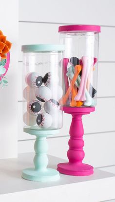 two glass jars with toothbrushes in them on top of a white shelf next to a flower vase