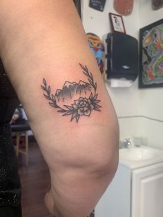 a woman's arm with a tattoo on it that has mountains and flowers in the middle