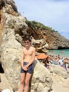 a shirtless man standing on the beach next to some rocks