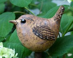 a brown bird sitting on top of a tree branch next to green leaves and flowers