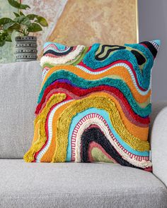 a multicolored pillow sitting on top of a couch next to a potted plant