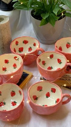 six pink bowls with strawberries on them are sitting on a table next to a potted plant