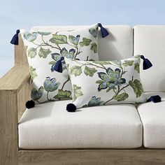 three pillows on a white couch with blue tassels and green leafy designs