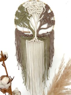 a white and brown dream catcher with trees on the front, surrounded by dried flowers