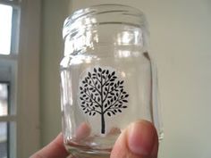 a person holding up a glass jar with a tree on the front and bottom, in front of a window